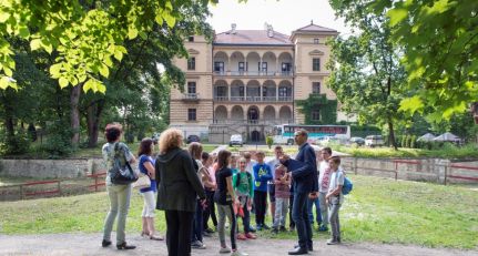 Fotografia: grupa dzieci w parku, w tle Willa Decjusza